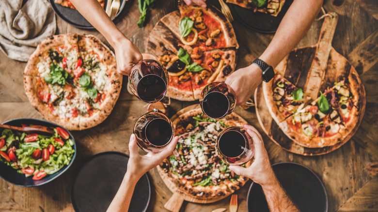 friends clinking wine glasses above pizza