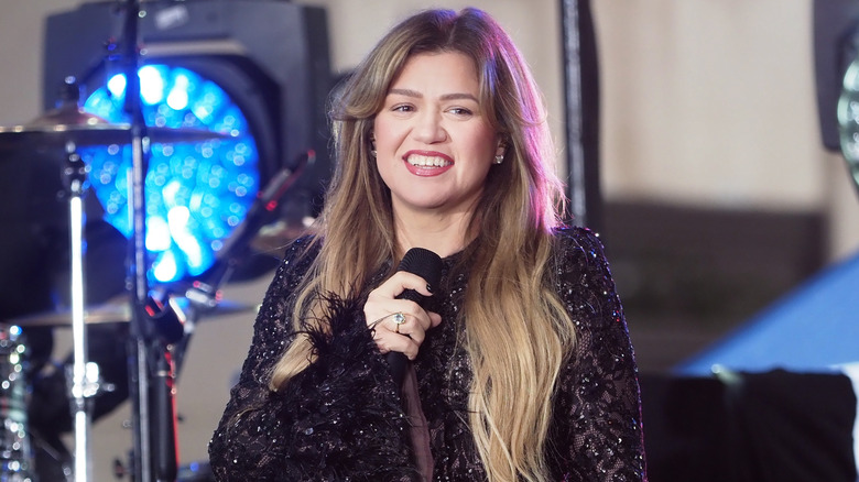Kelly Clarkson smiling while holding a microphone