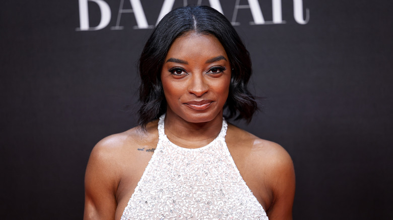 Simone Biles smiling for photos in a white halterneck dress