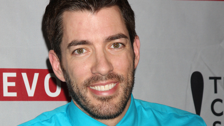 Drew Scott poses wearing a bright blue shirt and a smile
