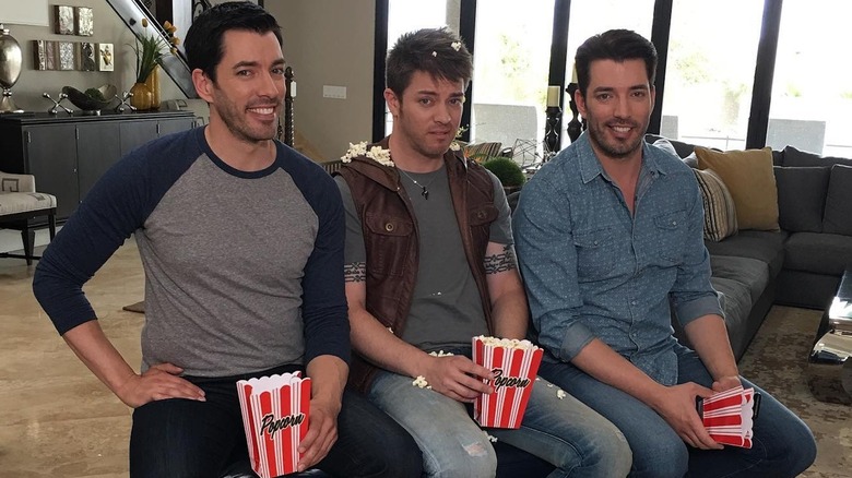 The Property Brothers and J.D. Scott sit smiling holding popcorn with popcorn spilled on J.D.