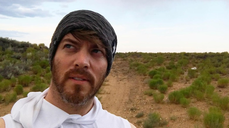 The third Property Brother, J.D. Scott, looks to the side in a beanie for a selfie on a dirt trail