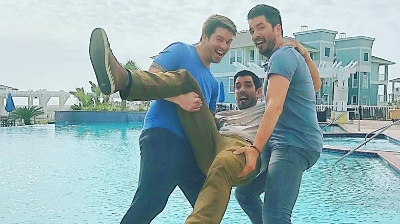The Property Brothers and J.D. Scott smile before throwing their brother into a pool