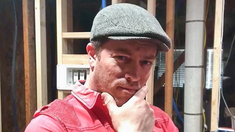 J.D. Scott in a hat poses with his hand on his chin