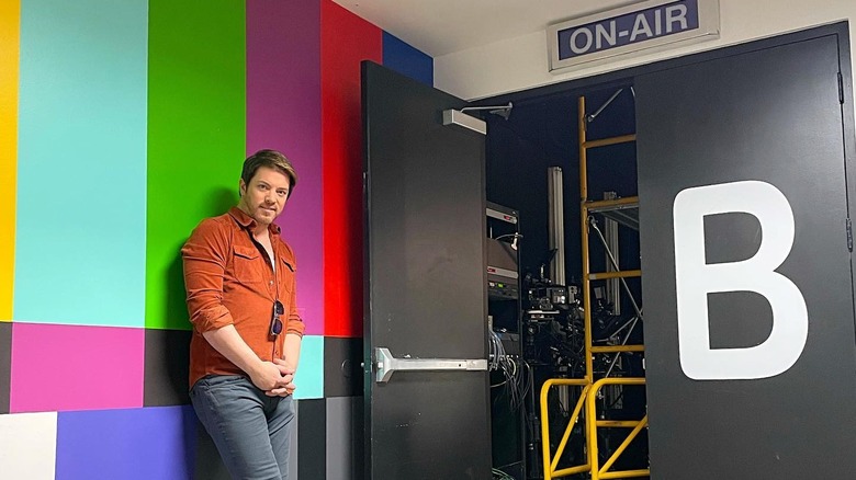 J.D. Scott poses leaning on the wall back stage near an "on-air" sign.
