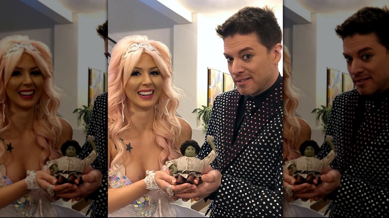 J.D. Scott and his wife Annalee Belle smile on their wedding day holding a spooky doll