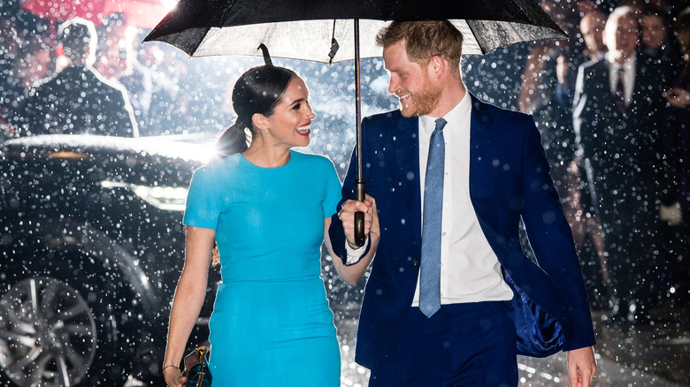 Meghan Markle and Prince Harry smiling at each other under an umbrella