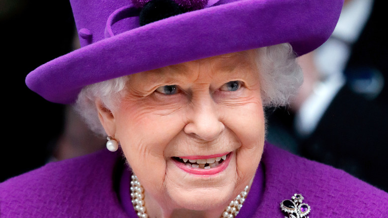 Queen Elizabeth II smiling in a purple hat