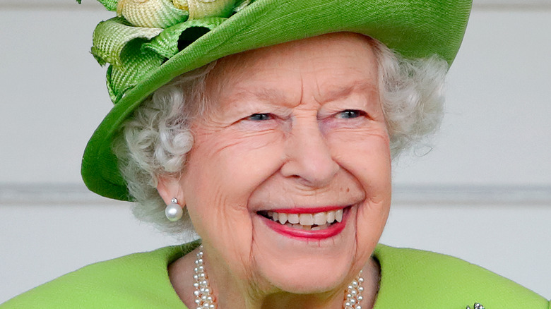 The queen smiling in a lime green outfit and pearls