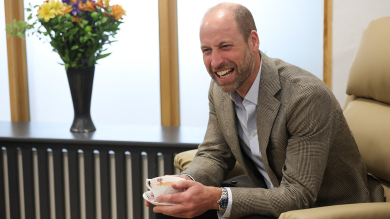 Prince William laughing while holding a cup of tea