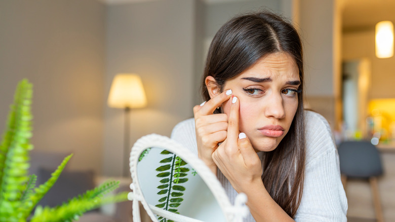 Woman's picking at zits looking in mirror