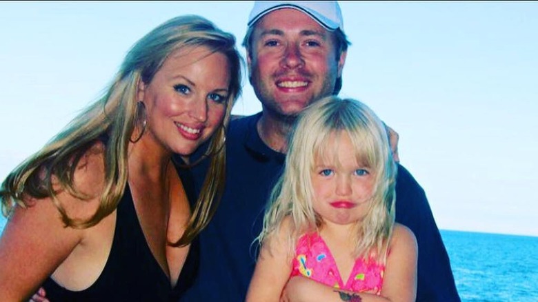 April Telek smiles in a picture next to her husband Jamie Campell and her daughter on vacation in front of water