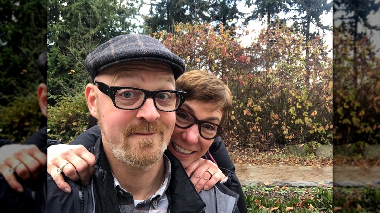 Janet Gigliotti smiles outside in front of trees in a selfie with her husband