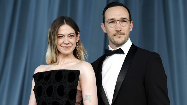 Lio Tipton and Chaz Salembier wearing black and standing in front of a blue curtain
