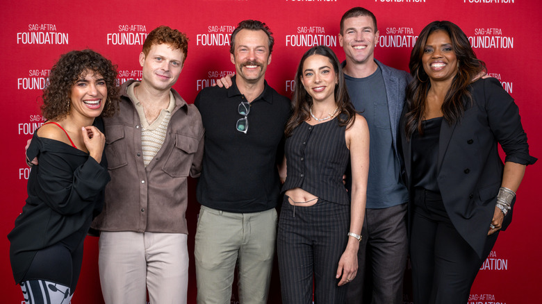 The cast of NCIS: Origins posing in front of a red background
