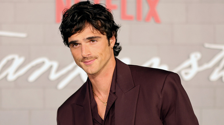 Jacob Elordi smiling for photos in a burgundy suit