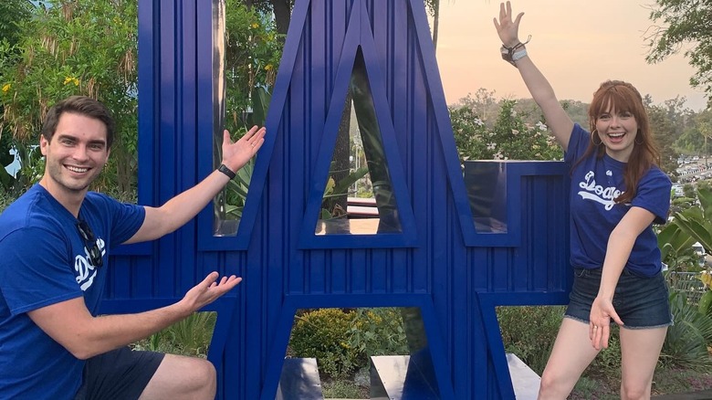 Cassidy Finch from "The Middle" smiling in front of a LA dodgers statue wearing a matching shirt with her husband