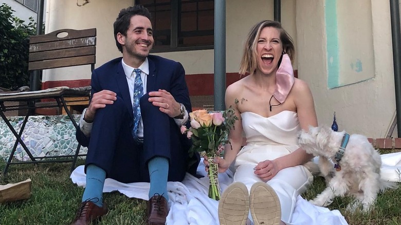 Eden Sher sitting with her husband and dog on the grass on their wedding day laughing