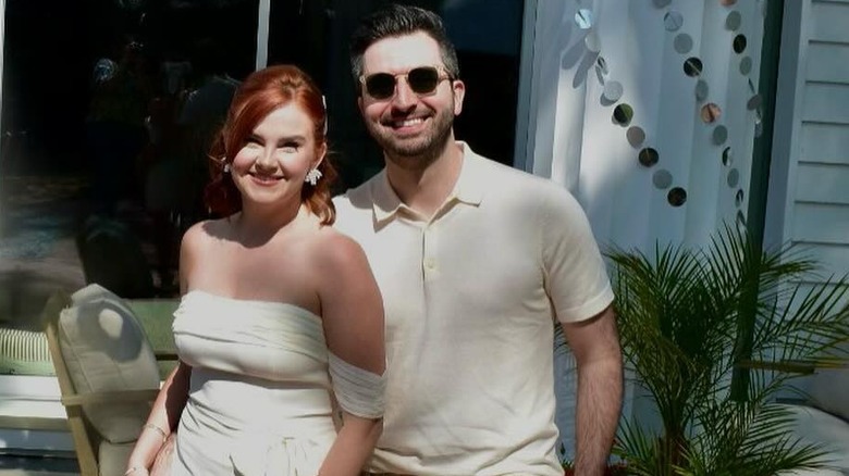 Actor Grace Bannon smiling outside in a white dress next to her husband
