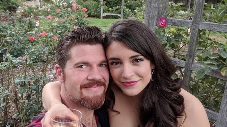 Actor Daniela Bobadilla has her arm around Beau Wirick holding a drink as they smile outside in a garden