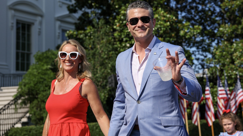 Pete Hegseth and Jennifer Rauchet holding hands as they walk in the street wearing sunglasses