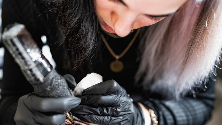 Woman tattooing client's arm 