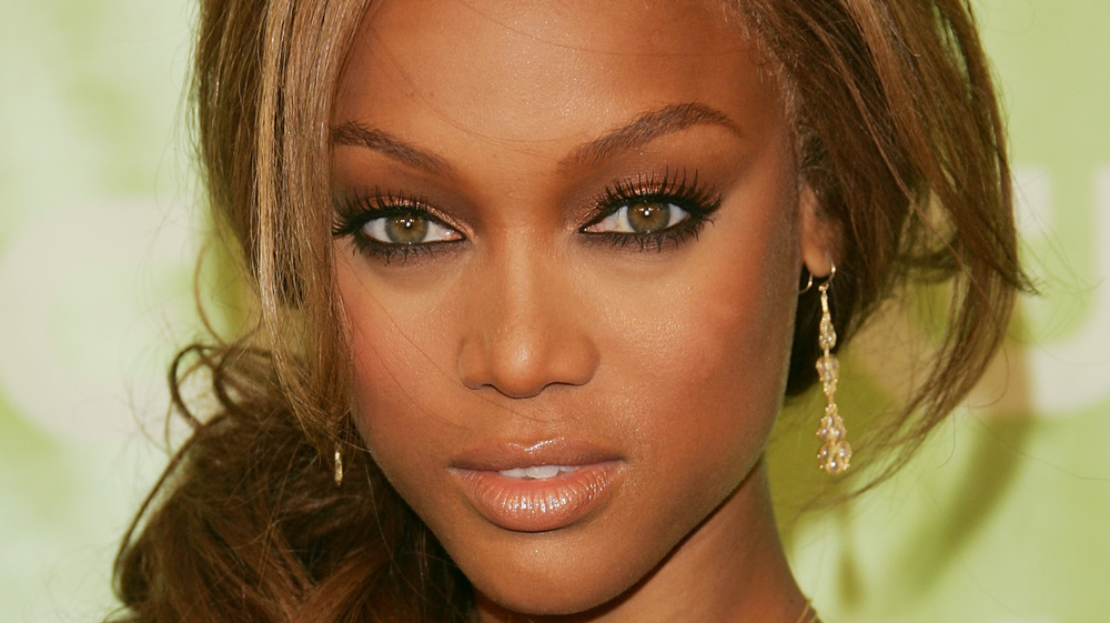 Close up of Tyra Banks in gold tones makeup against a green background