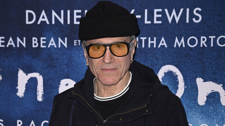 Daniel Day-Lewis posing while wearing a black beanie and orange glasses on the red carpet