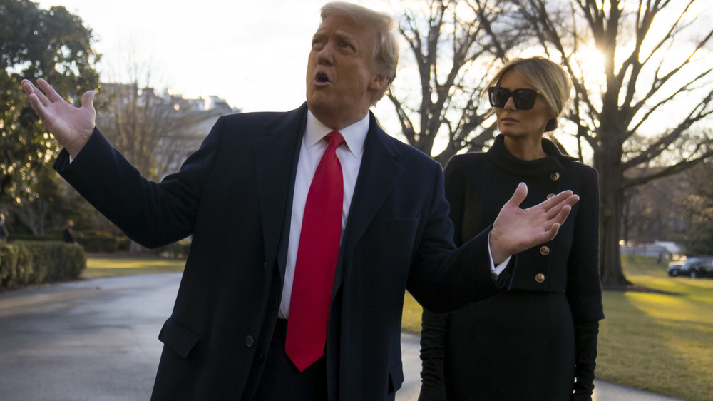 Donald Trump with arms wide open in red tie with Melania Trump in dark sunglasses