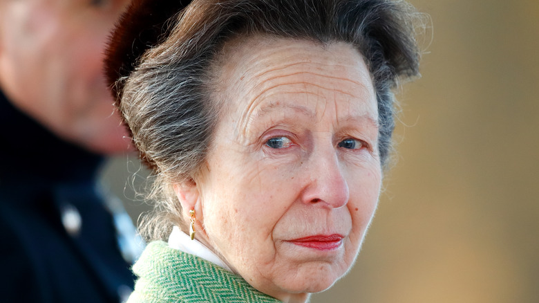Princess Anne wearing a green jacket with her hair pulled back looking over her shoulder at the camera