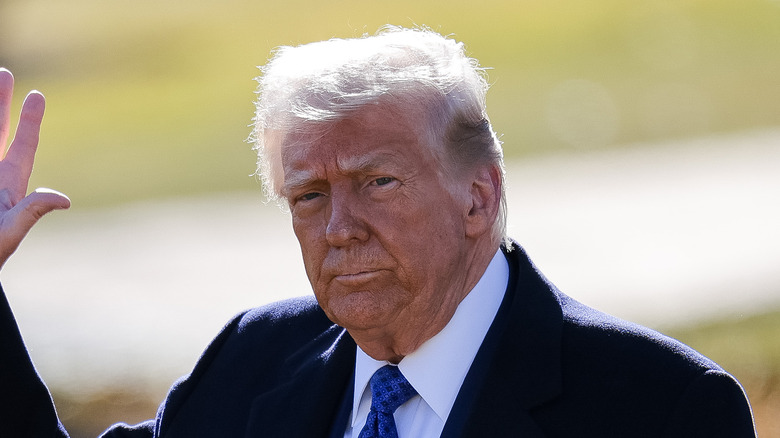 Donald Trump leaving the oval office while wearing a black trench coat and blue tie.
