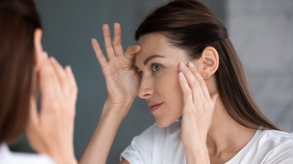 A woman inspects her face in a mirror 