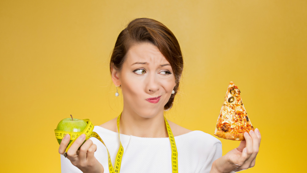 Woman feeling guilty between pizza and an apple