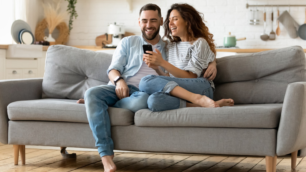 Happy couple looking at a smartphone on the couch.