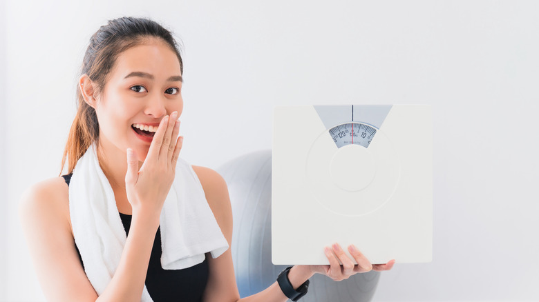 A woman smiling while holding a weighing scale 