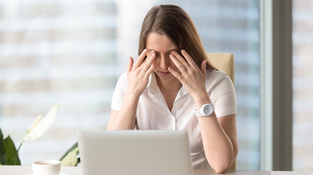 Woman sitting at computer touching her eyelids