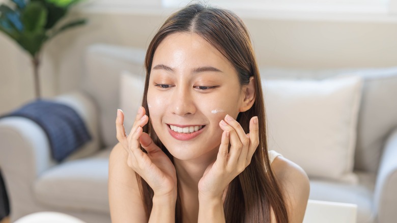 Woman applying makeup primer to her face