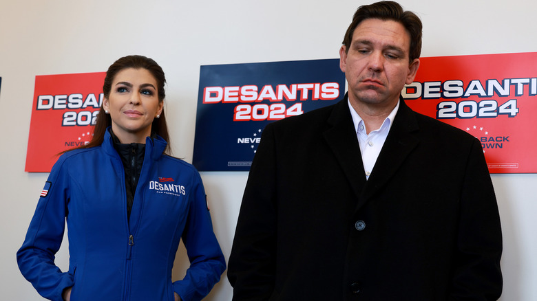 Casey DeSantis and Ron DeSantis standing in front of campaign posters