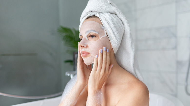 Woman sitting in tub with sheet mask on