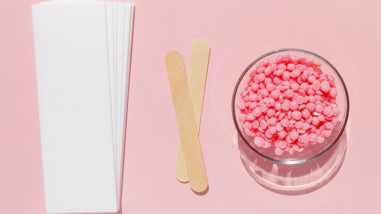 Hard wax beads next to applicator sticks and cloth waxing strips