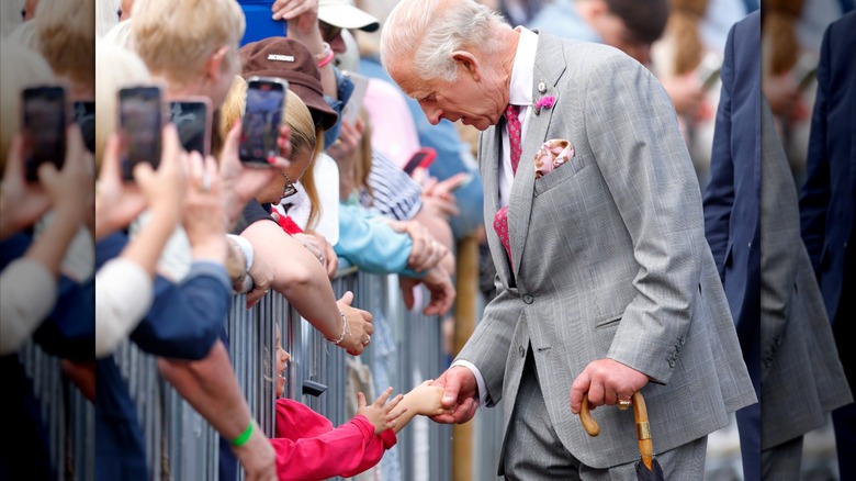 King Charles greeting children in crowds while holding an umbrella