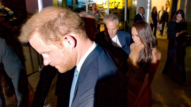 Meghan Markle and Prince Harry surrounded by fans and being escorted by security