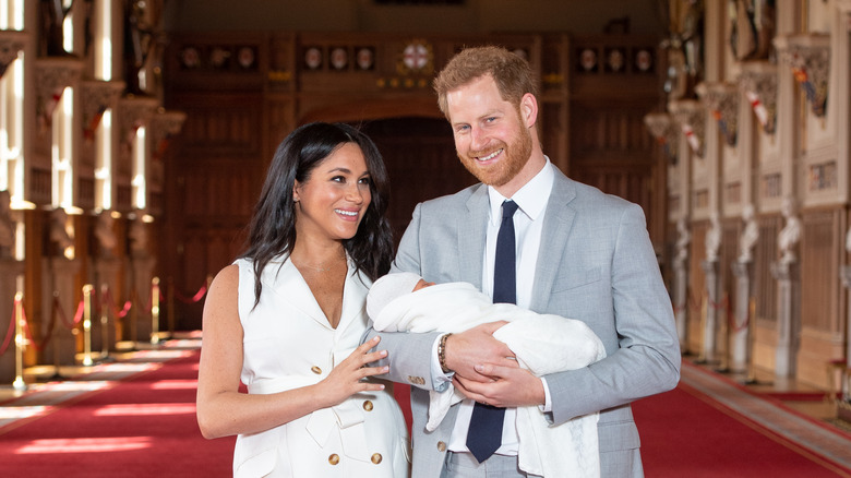 Meghan Markle stands next to Prince Harry holding Prince Archie