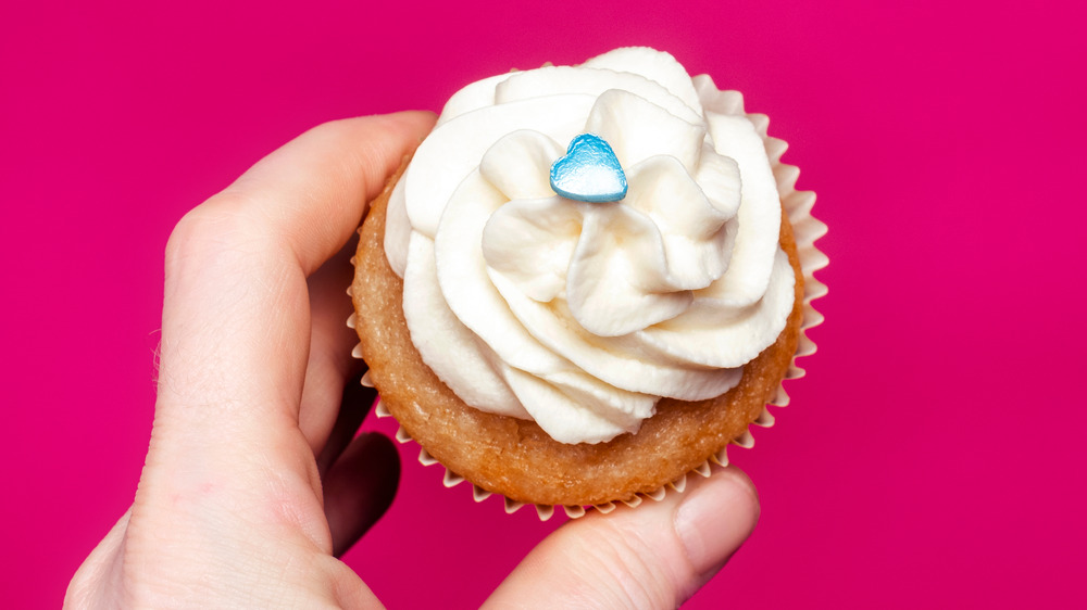 A cupcake is seen with vanilla icing and a blue heart