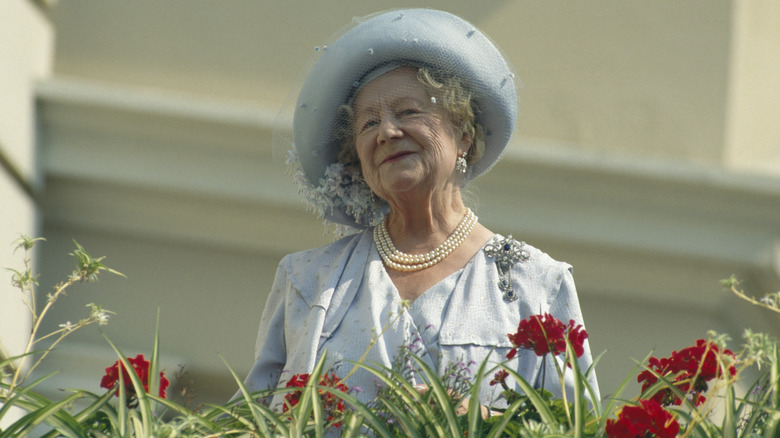 The Queen Mother smiling from a balcony while wearing a coordinated blue outfit with pearls.