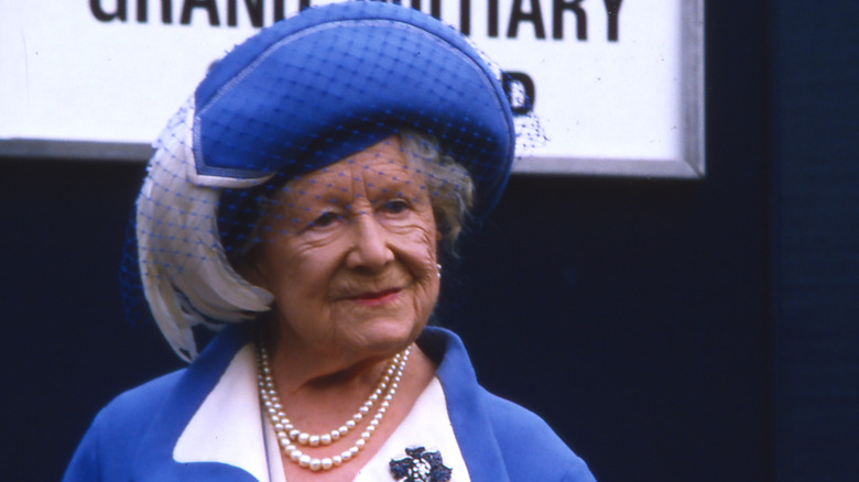 The Queen Mother wearing a matching blue hat and coat with a pearl necklace.