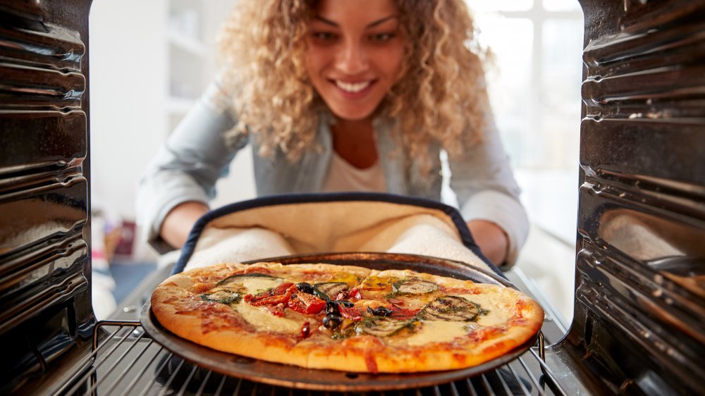 Woman taking a cooked pizza out of a home oven