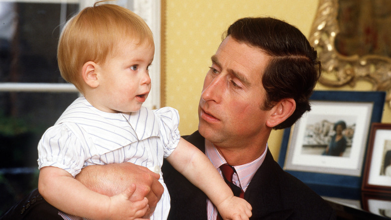 Young King Charles III holding baby Prince Harry