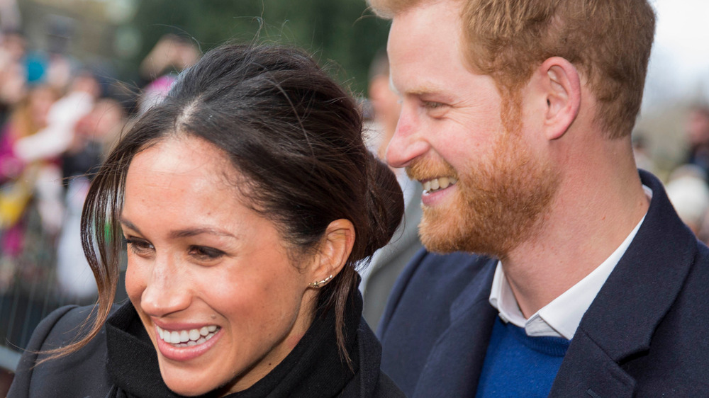 Prince Harry and Meghan Markle smiling while greeting fans