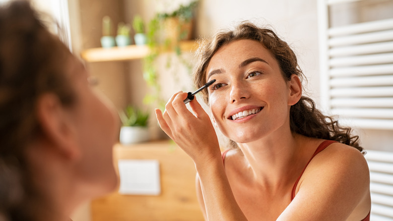 A woman applying mascara while smiling 